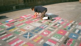 A man draws the flags of many nations using sidewalk chalk