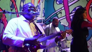 A musician, wearing a white shirt, sings passionately into a microphone on stage.