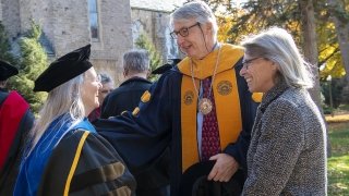 Grant Cornwell, wearing academic regalia, greats a Saint Lawrence professor.
