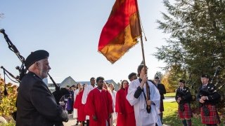 A group of Saint Lawrence students, holding a scarlet and brown flag, walk past bag pipers during the presidential inauguration ceremony at Saint Lawrence University.