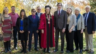 Saint Lawrence University President Kathryn Morris, wearing scarlet presidential regalia, stands with her family on a sunny fall day.