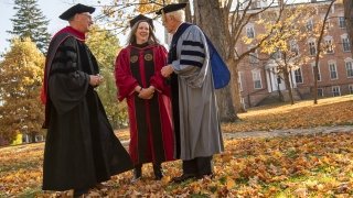 Saint Lawrence University President Emeritus William Fox, President Kathryn Morris, and President Emeritus Dan Sullivan, wearing academic regalia, laugh while standing outside on a sunny fall afternoon.