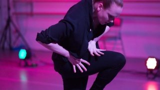 A woman in black dances in a studio filled with pink light