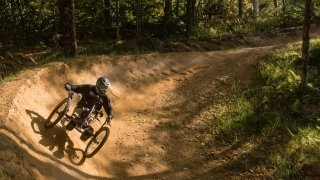 A person rides an all terrain bicycle on a dirt trail in the woods. 