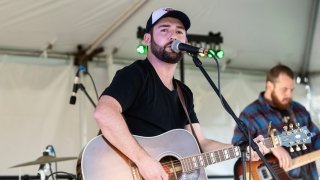 Blaine Holcomb, playing a guitar, sings into a microphone on stage.