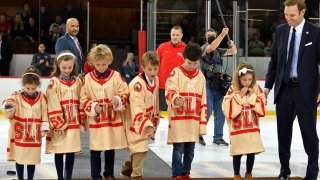 The grandchildren of Joe Marsh, wearing custom Legends jerseys, drop their pucks on the ice while Scott Lasky ’05, Hockey Alumni Association Executive Board chairman and co-chair of the Legends Selection and Planning Committee, cheers them on.