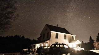 The starry night sky over a white farm house. 