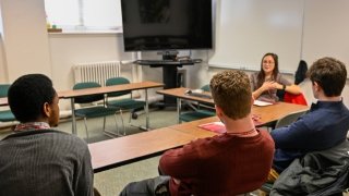 Three people sit a a table facing a speaker during a small group discussion.