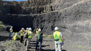 A group of students wearing neon yellow construction vests and white helmets stand in a volcano structure.