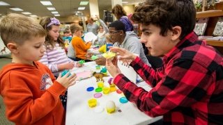 A group of young students talks with college-aged students while working with Play-Doh.