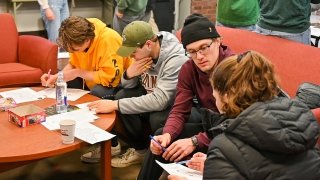 Four students sit on a red couch and appear focused as they write on paper during a math competition.