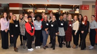 Several Laurentians, wearing business casual attire, stand together and smile at Appleton Arena as part of the Saint to Saint Women's Summit.