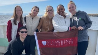A group of Saint Lawrence University students hold a scarlet and brown flag on a boat. 