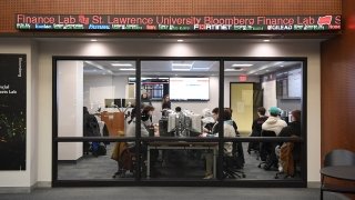 Looking into the Bloomberg Finance Lab, which is embedded in the library and visible through large windows. There's a stock ticker above the windows.