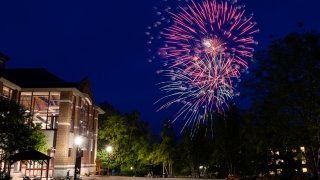 The Sullivan Student Center glows under lamp posts as fire works burst in the night sky.