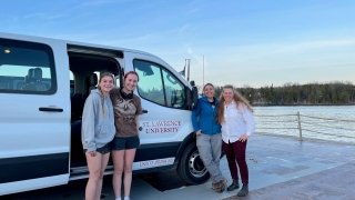 two female students and two female faculty standing next to SLU Van on fairy