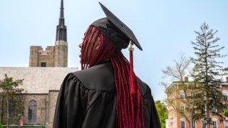 Sarath Novas, her hair in long, red braids, wears her full graduation regalia, including her cap and gown. Photo is of the back of her head as she looks forward inspirationally.