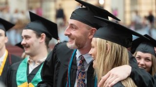 A grad puts their arm around a classmate and smiles for a photo.