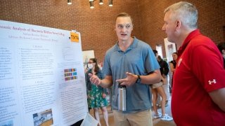 Nathan Rosachc stands in front of his biology research poster and explains his project to Matt Carotenuto.