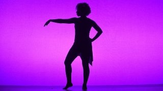 A black silhouette of a dancer stands in front of a magenta and purple screen.