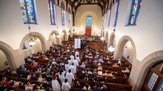 Students wearing white robes file into Gunnison Memorial Chapel where the pews are filled with attendees.