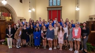 A large group of students gather at the front of Gunnison Memorial Chapel and smile.