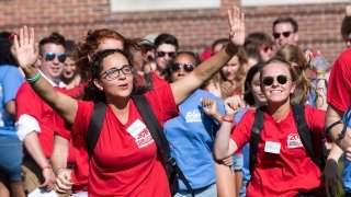 Saint Lawrence orientation leaders, wearing scarlet shirts, celebrate the incoming class on a sunny day. 