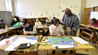 Obiora Udechukwu helps a Saint Lawrence student working on an art project. Several students are busy working on their own projects in the background.