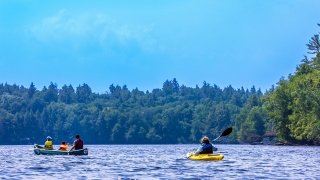 Four people in two kayaks paddle across the upper saranac lake.