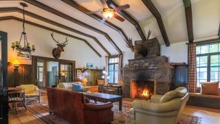 A large lodge style room with a roaring fire place and a large moose head and deer head mounted on the wall.