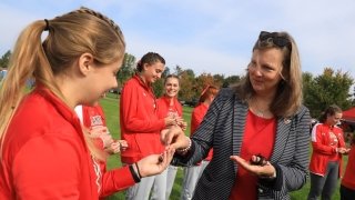 President Morris hands lady bug bracelets to smiling members of the Saints Women's Cross Country Team.
