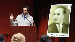 Steve Peraza stands at a podium while delivering a talk next to a large, blown-up yearbook image of Jeffrey Campbell.