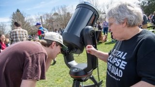 Aileen O'Donoghue, wearing a black Total Eclipse of the Quad t-shirt helps a student as they peer into a large black telescope.