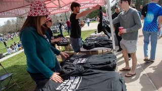 A group of people stand behind a table and hand out black total eclipse of the quad t-shirts to students.