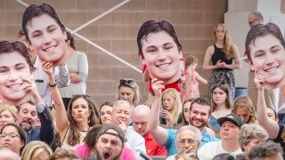 Photo of the crowd, with multiple people holding up large printed signs of a students face. Lots of excitment adn clapping as they cheer for the studnet who was walking the stage.