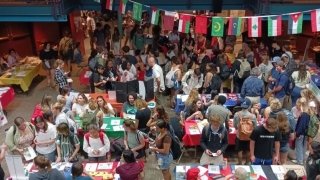 A large group of people gather in the Student Center talking to one another, with flags in the background