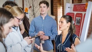 Students present their research on Formula 1 data visualization to attendees during an academic poster session at Saint Lawrence University, with visitors listening and taking notes.