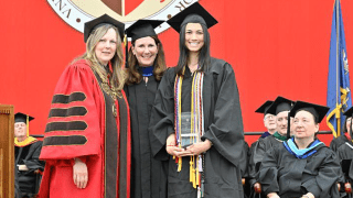 President Morris, Jennifer Curley Reichart, and Lily Kendall, wearing graduation regalia, stand at the podium during Saint Lawrence University's Commencement.