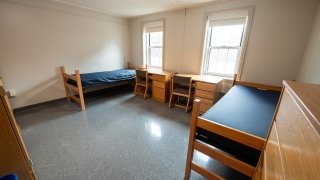 A double room in Gaines Hall includes two beds, two desks with chairs, and two dressers. Neutral walls and tile floors keep the space simple and easy to personalize. Large windows provide plenty of natural light.