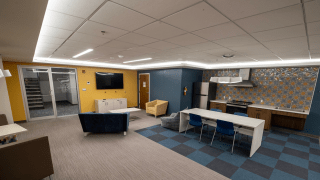 Lounge in Lee Hall with a kitchen, dining table, soft seating, and a wall-mounted TV, featuring colorful walls and tiled backsplash.