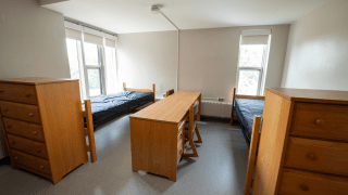 Double room with two beds, two desks, and two dressers, featuring neutral walls and large windows for natural light.