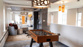 Lounge area with a foosball table, modern lighting, soft seating, and a fireplace with dark tile accent wall.