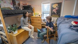 Two students talk inside a Saint Lawrence University dorm room with lofted beds, desks, plants, and string lights decorating the space.