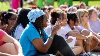 A group of students sitting outside on a sunny day, smiling and clapping during an event at Saint Lawrence University.