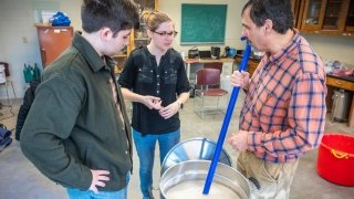 Joe Erilichman and two Saint Lawrence students stand around a large silver bucket brewing beer.