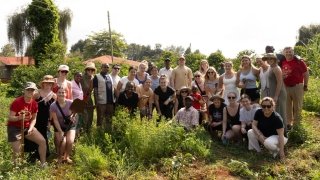 A group of smiling people gather together outside on a sunny day in Kenya.