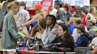 Students sit and stand at a crowded outdoor table during a campus event at Saint Lawrence University, chatting and smiling while surrounded by gear and club materials.