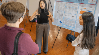 A student presents her research poster to her peers at a crowded campus event.