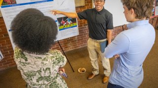 A student presents his research poster to his peers at a crowded campus event.
