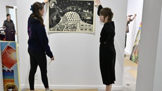 Students hang artwork in a gallery space during exhibition setup.
